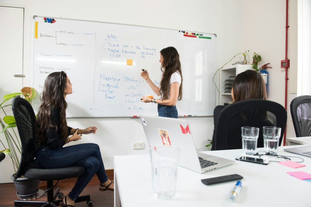 Trois collègues collaborent lors d'une session de brainstorming devant un tableau blanc rempli de notes et de stratégies marketing. Une atmosphère de créativité et de travail d'équipe prévaut, illustrant l'importance de la collaboration en entreprise pour développer des solutions innovantes.